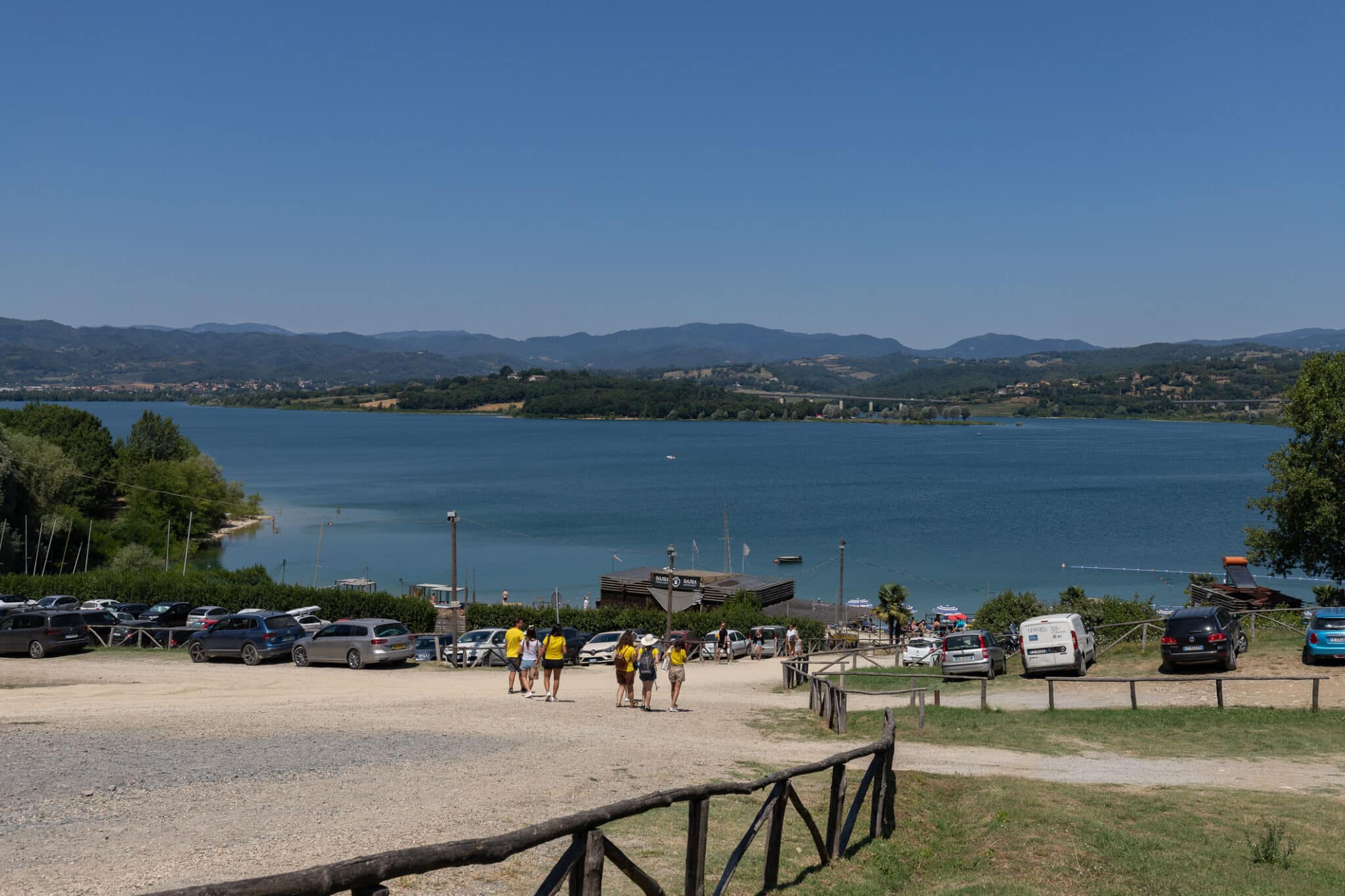 Lago tra colline, persone e parcheggio estivo