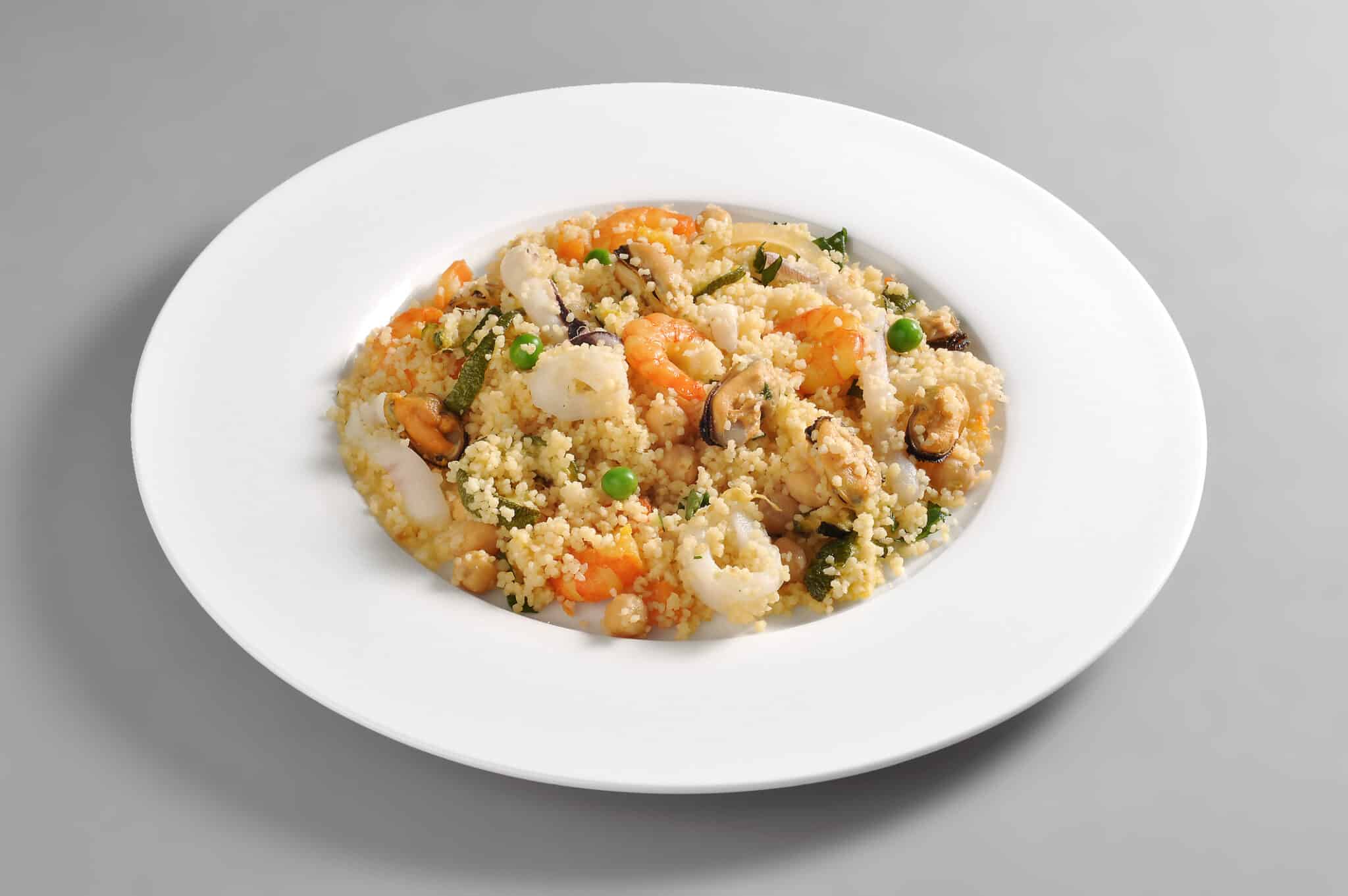 Couscous con gamberi, piselli e calamari su piatto bianco