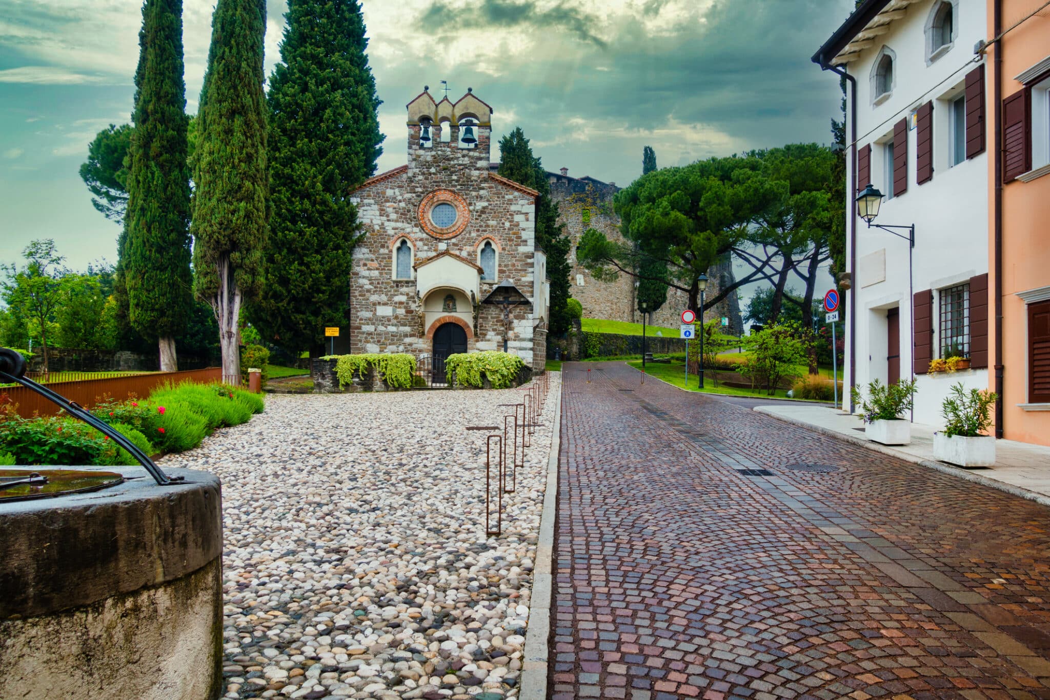 Chiesa storica in strada acciottolata circondata da verde.