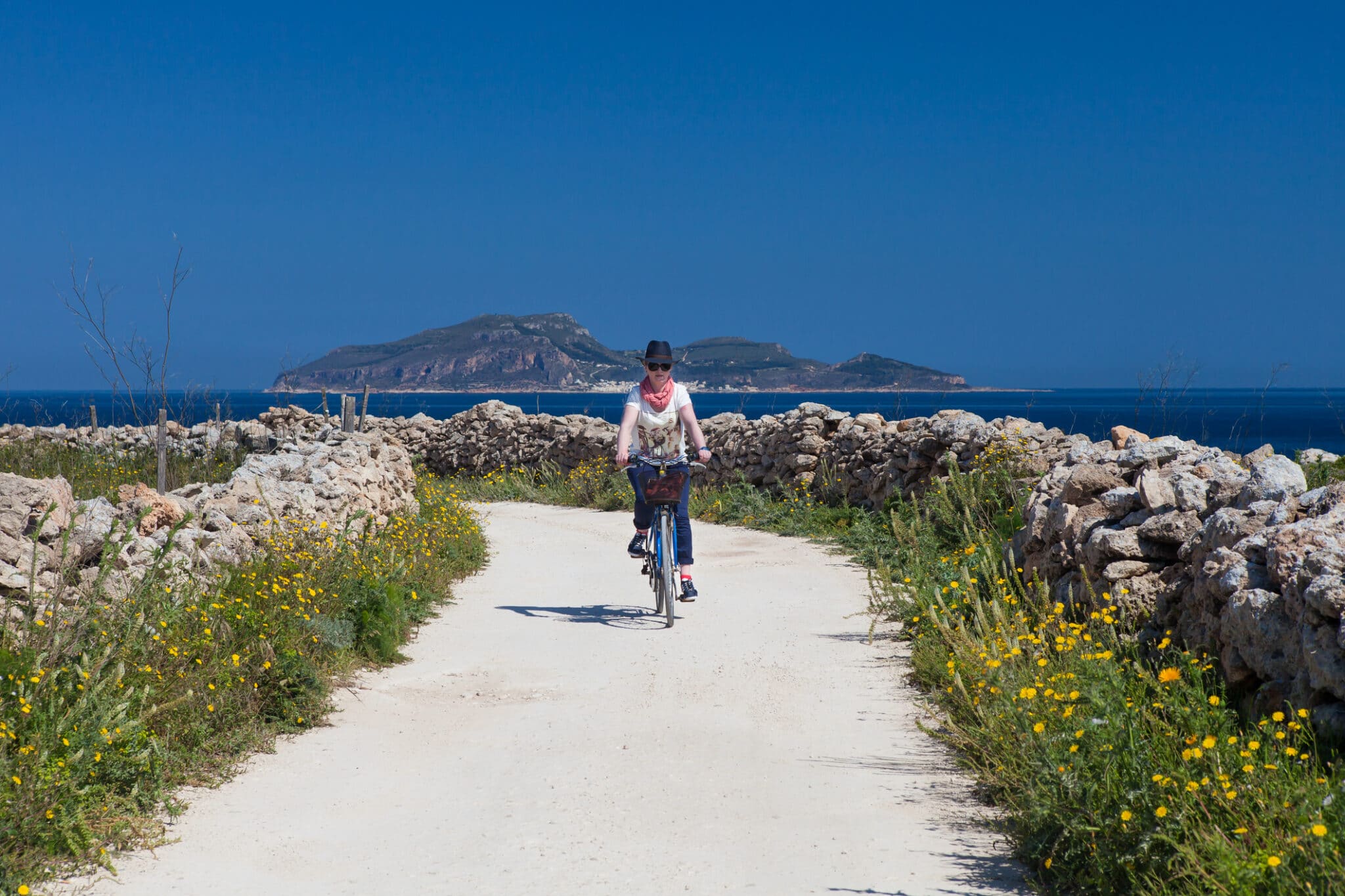 Donna in bicicletta su strada rurale, paesaggio mediterraneo
