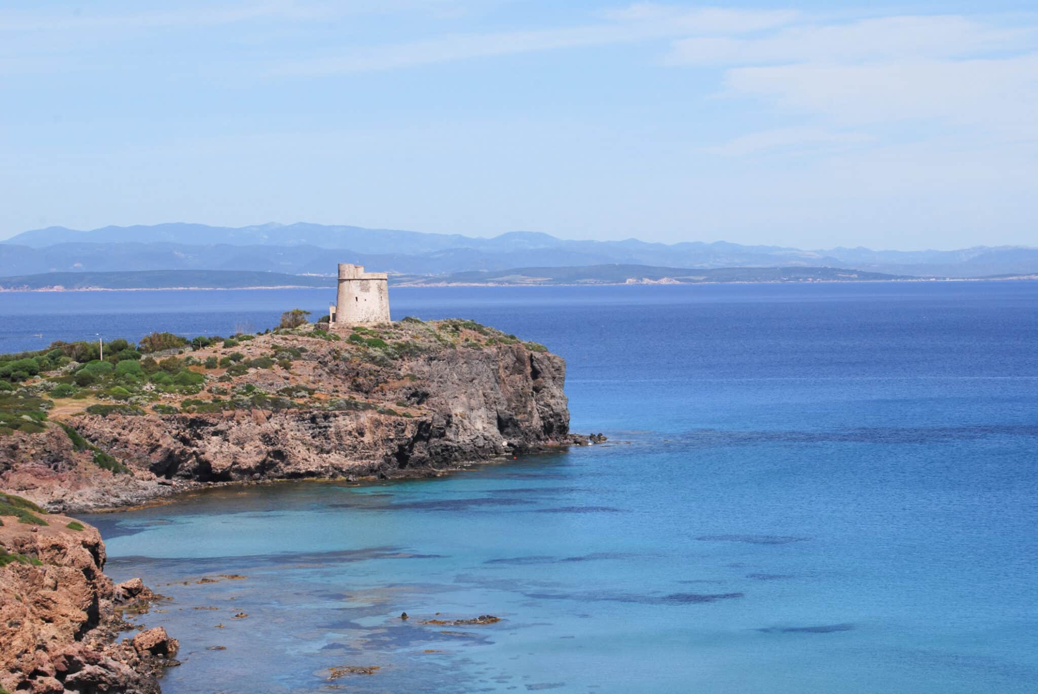 Torre costiera su promontorio, mare blu, cielo sereno