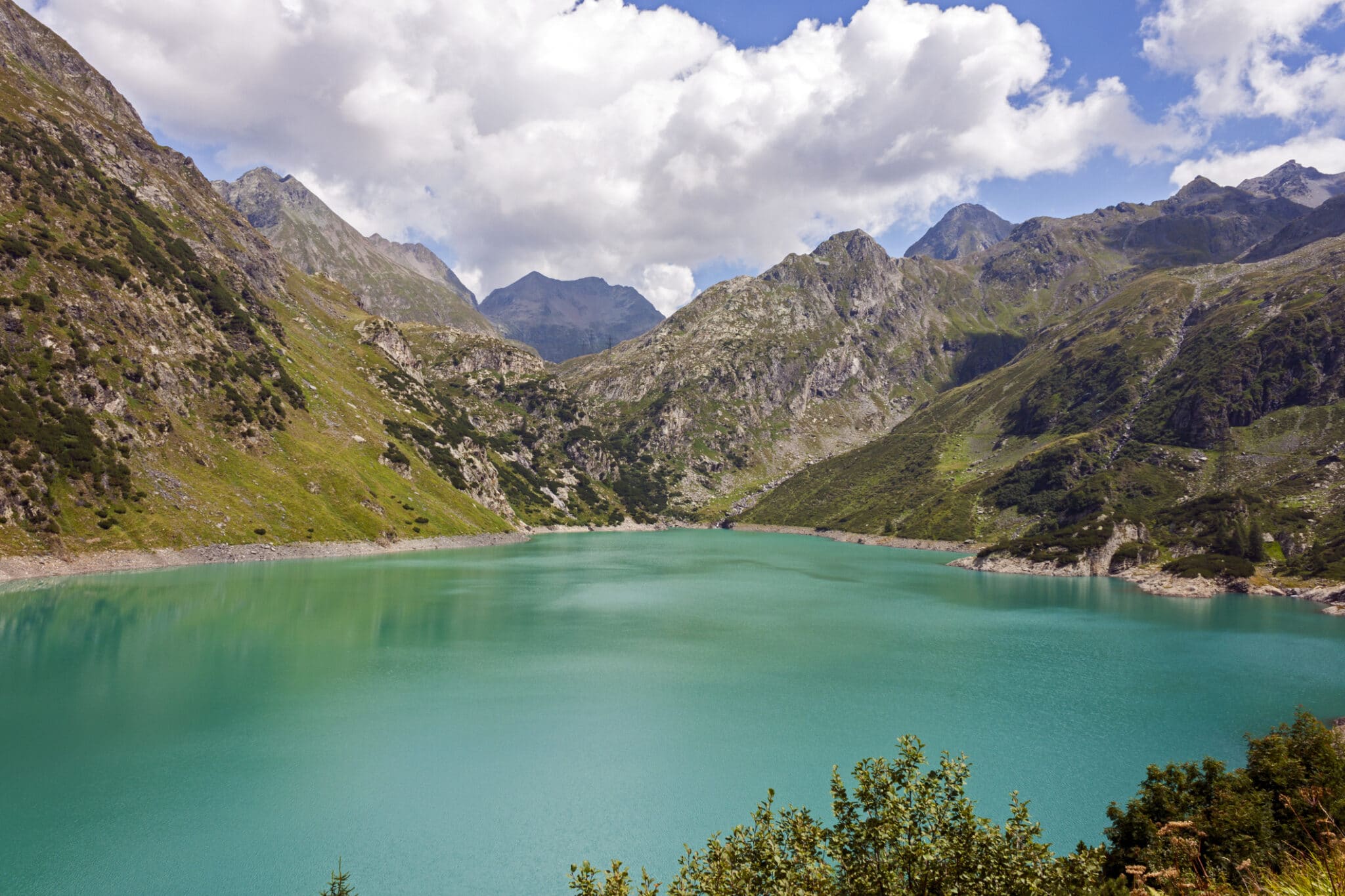 Lago alpino circondato da montagne verdi e cielo nuvoloso