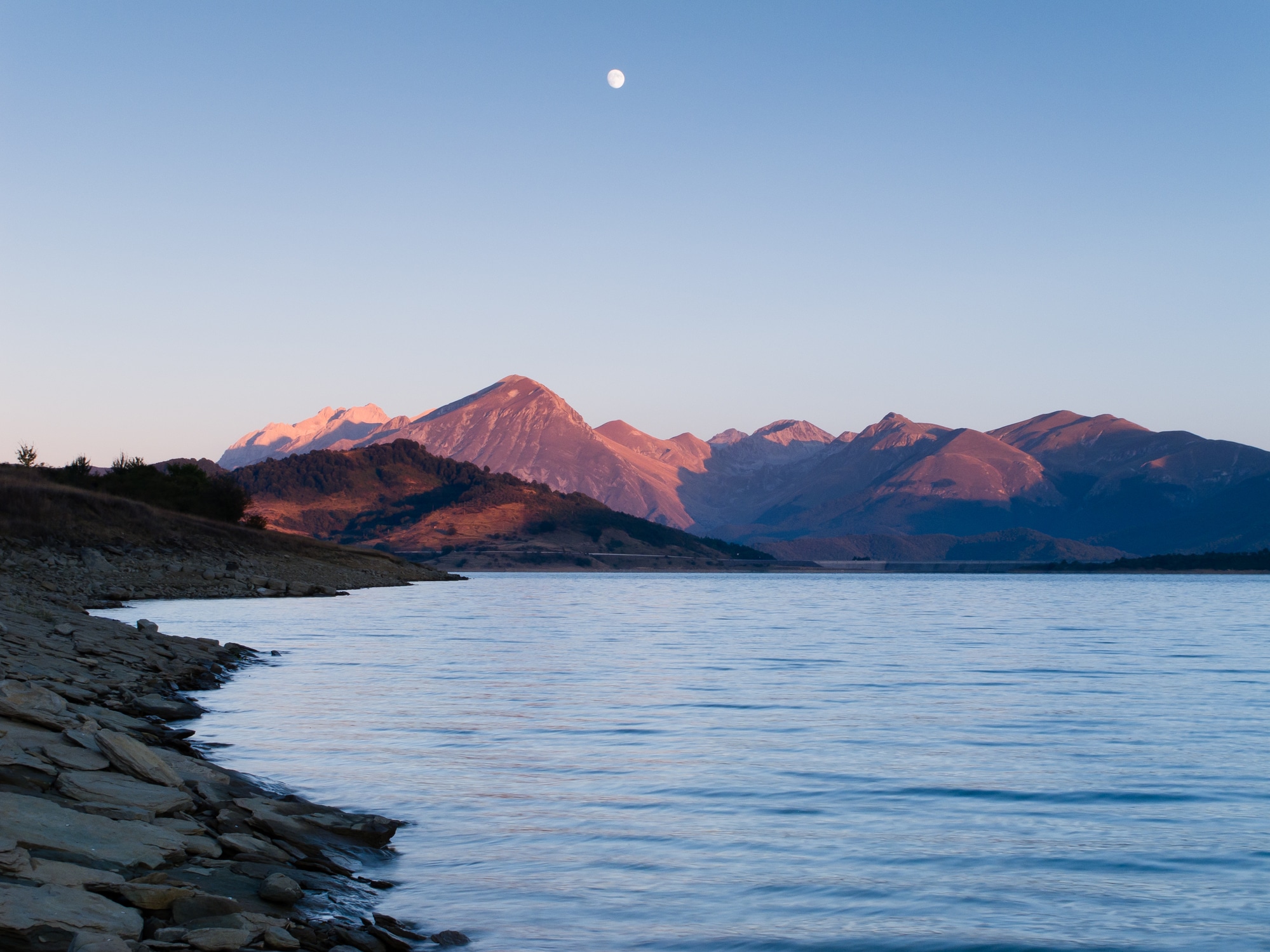 Montagne al tramonto con luna e lago
