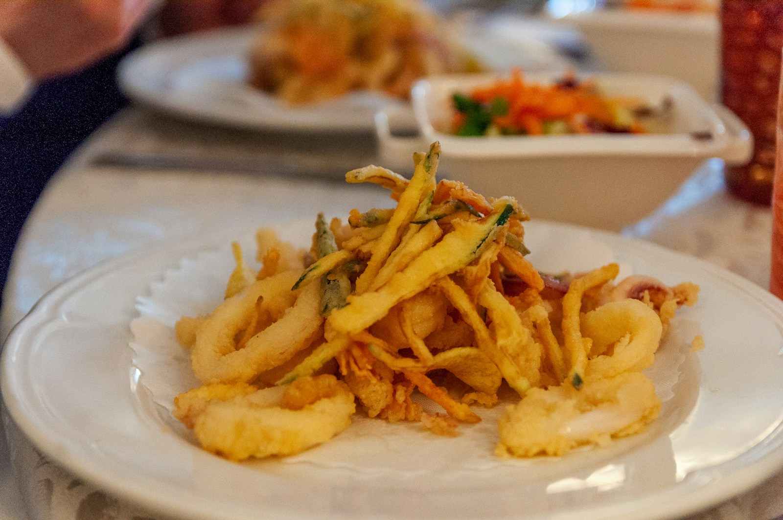 Frittura di paranza con anelli di calamaro e verdure croccanti servita su piatto bianco.