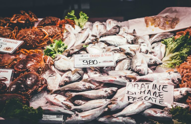 Bancarella di mercato con orate fresche e crostacei esposti su ghiaccio, pronte per la vendita.